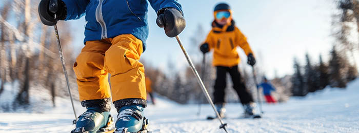 Snow sports safety for children skiing on a groomed winter mountain trail wearing helmets