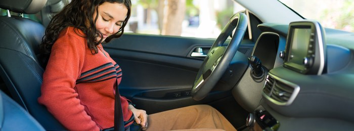 Teen driver buckling her seat belt, a key back to school safety habit.