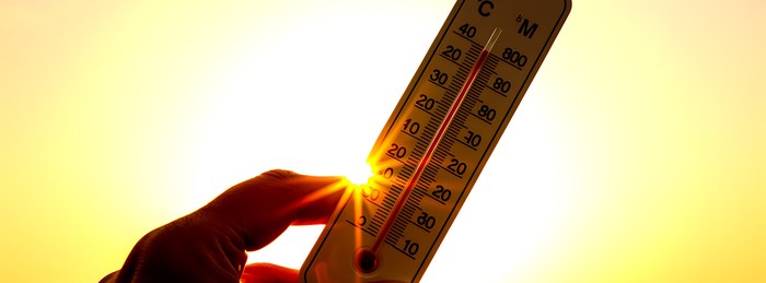 Thermometer held against a blazing summer sun during extreme heat safety season.