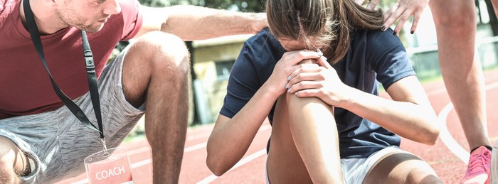 Coach checking on a young athlete showing signs of distress at practice.
