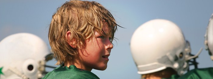 Young football player on the sideline during a hot practice, a fall sports safety concern.
