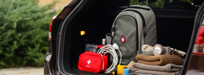 Emergency supply kit with a first-aid bag, flashlight, rope, and blankets packed in a car.