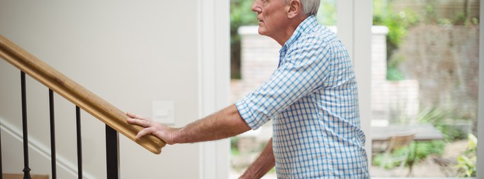 Older adult using a handrail on well-lit stairs during Falls Prevention Awareness Week.