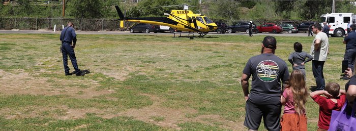 Bystanders watching from a distance as a PHI Air Medical helicopter waits on a landing zone.