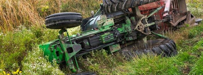 Overturned tractor lying on its side in a ditch with the cab structure intact.